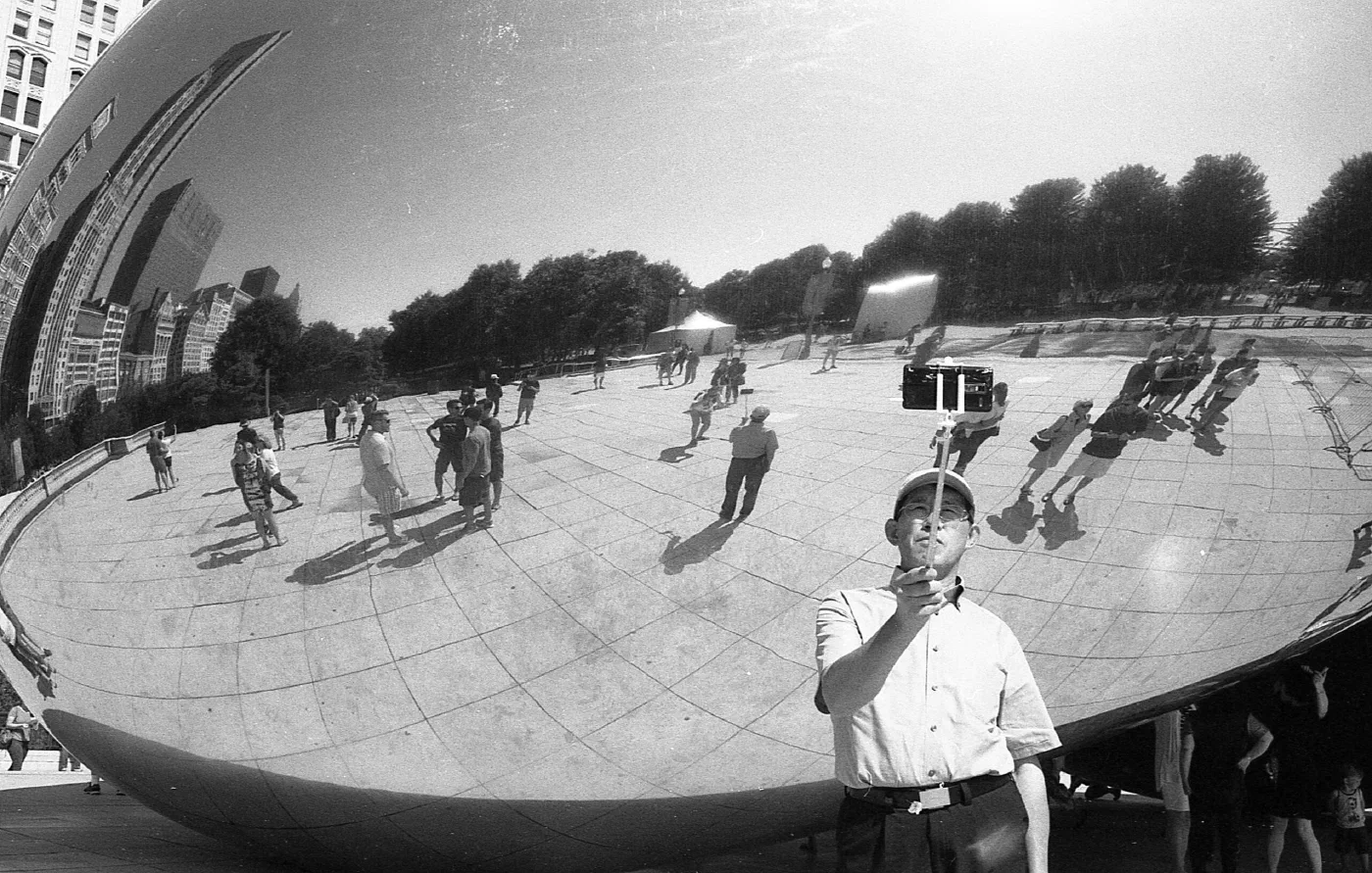 Reflection of a person with a selfie stick against the Chicago Bean